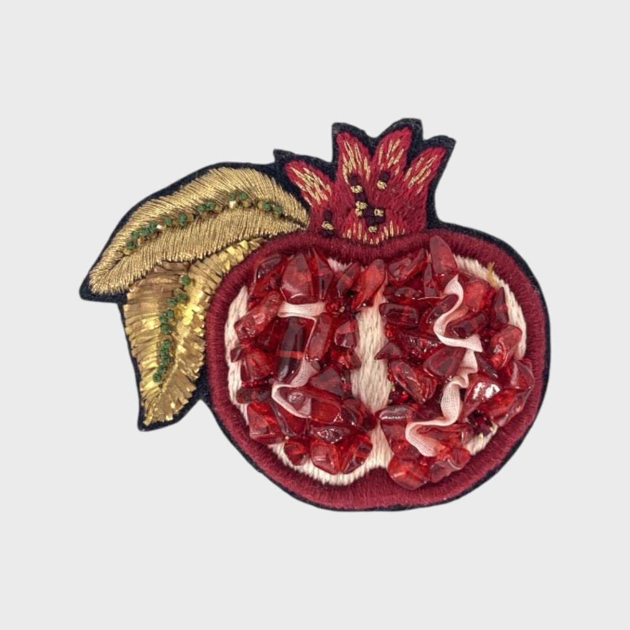 An embroidered brooch representing a grenade with red, white and golden details.