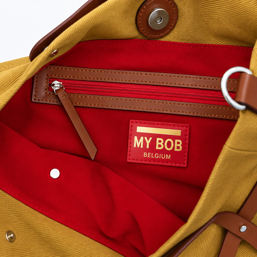 Detail photo of the inside of the optimiste mustard bag with a red velvet lining and a red zipper with cognac brown leather trim. Showing the MY BOB logo underneath.