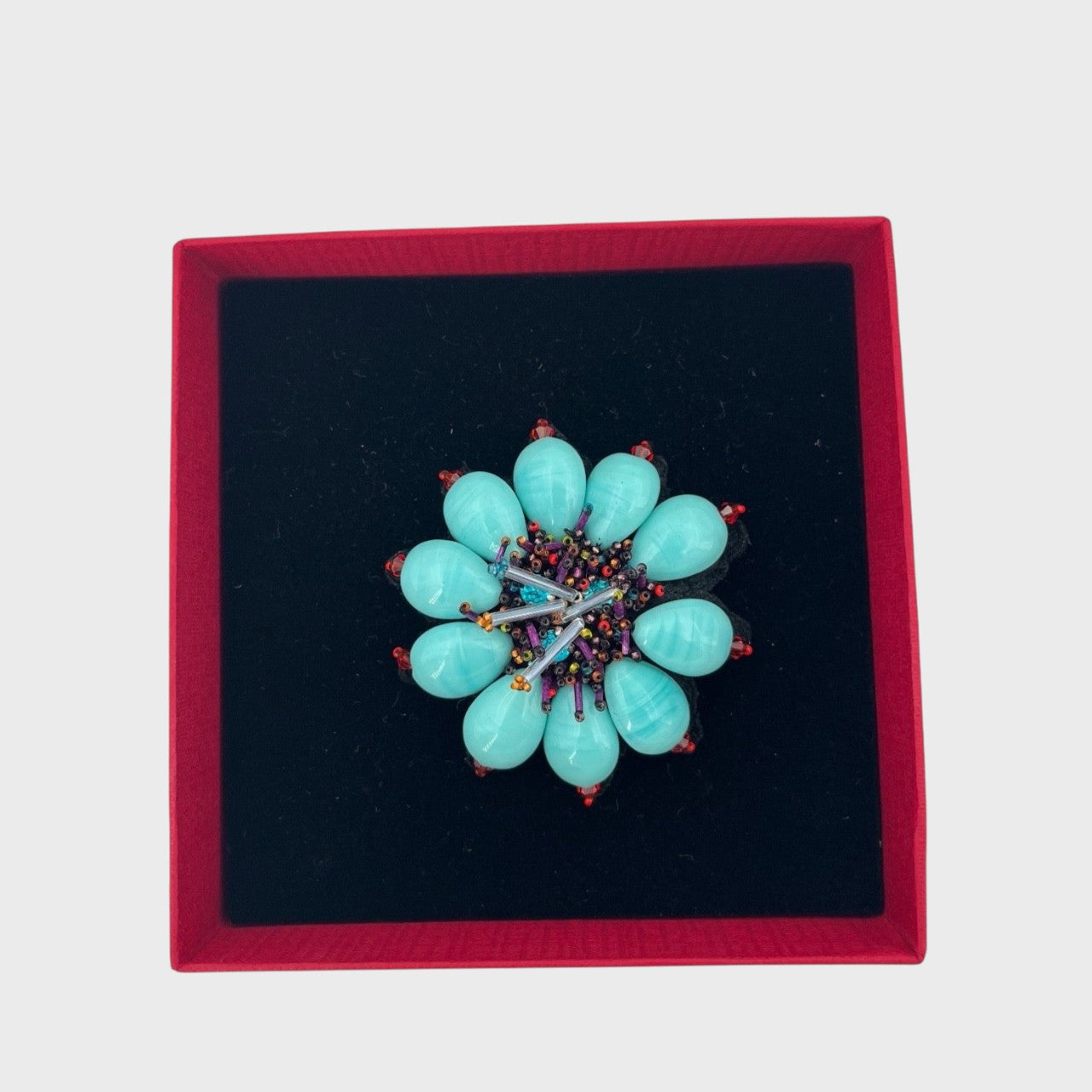 An embroidered brooch representing an blue ixia flower in a box.