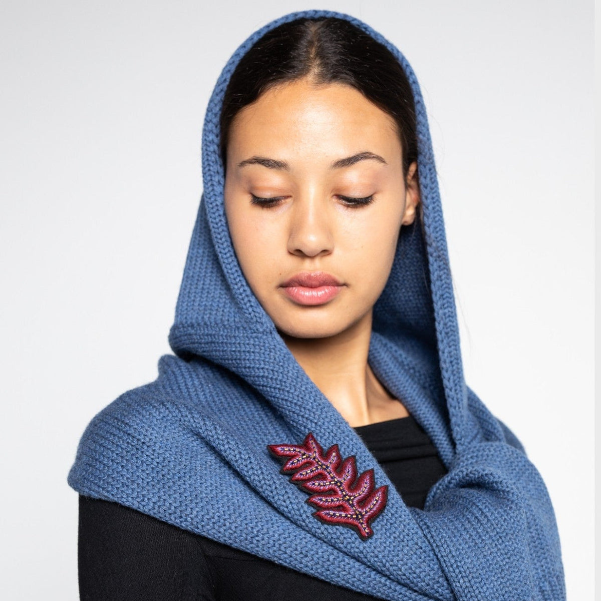 Woman wearing a blue wool hat scarf with a floral brooch on a white background