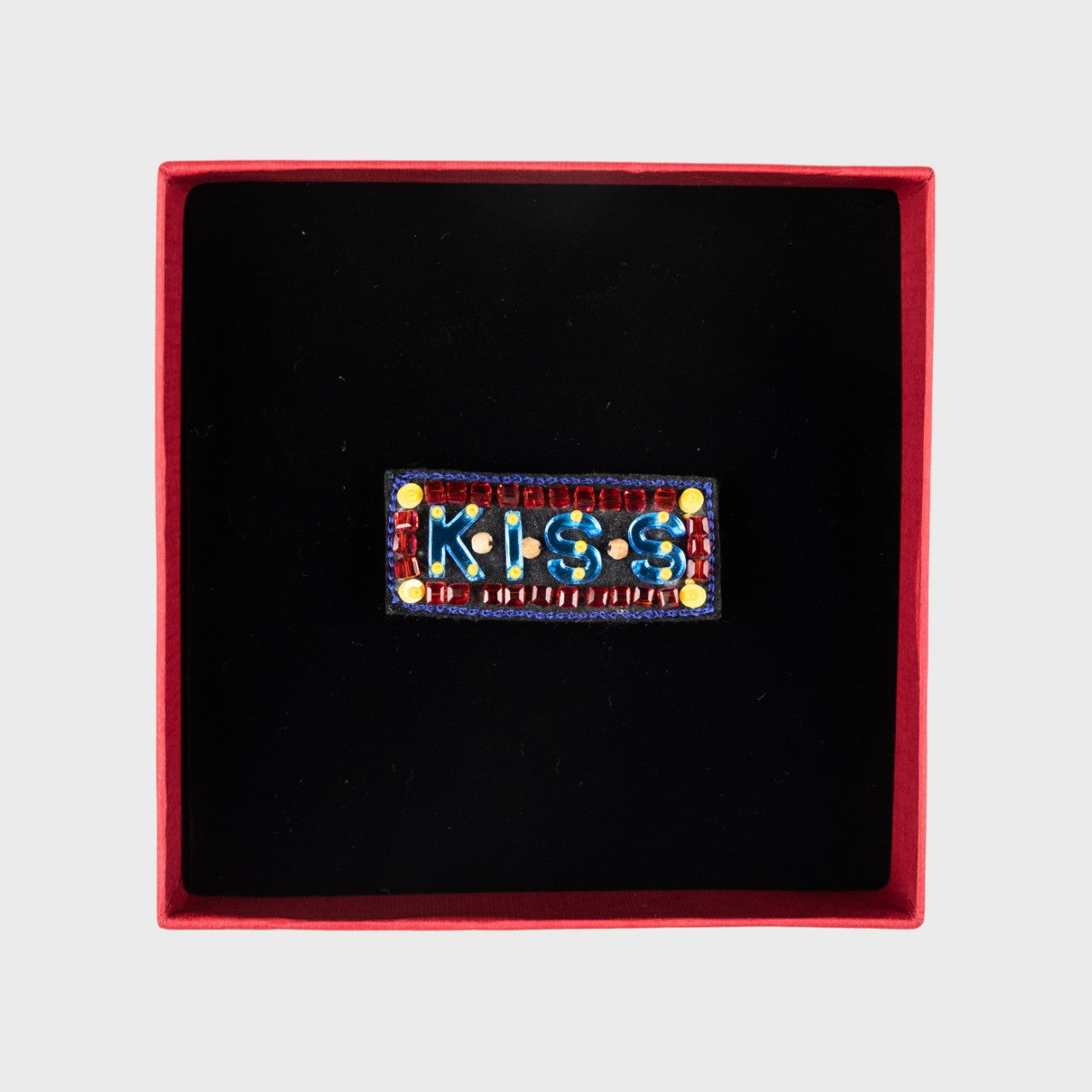 An embroidered blue KISS Brooch with a box.