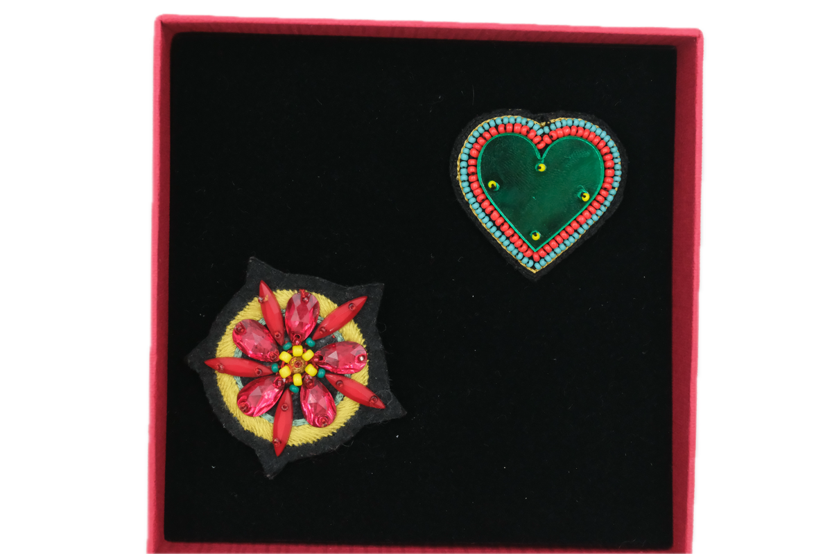 Two embroidered brooches, one shaped like a heart, the other representing a flower in a red box.