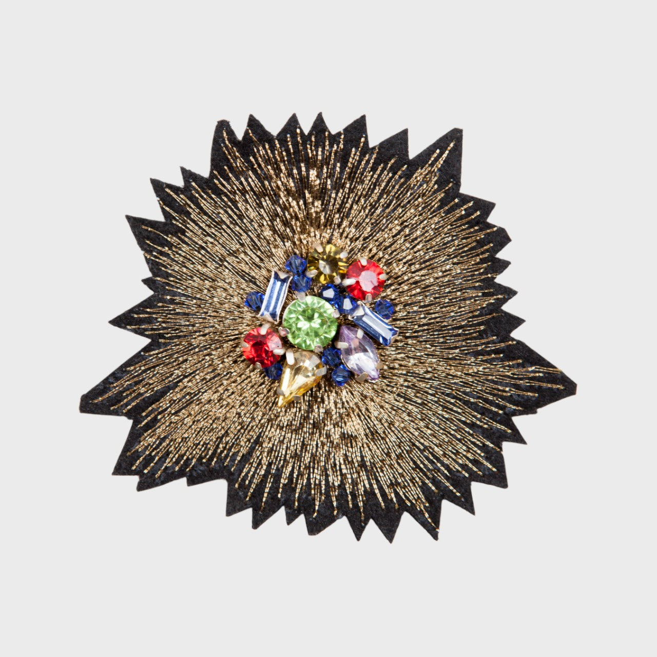 An embroidered brooch representing the golden sunset with blue, red, yellow and green stones in the middle.