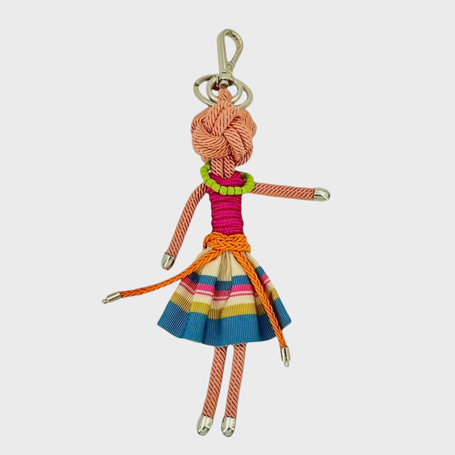 Handmade tan macramé bag charm featuring a female character, wearing a striped blue and white mini skirt paired with an orange belt, a short sleeves pink top and a green beaded necklace. She is attached to a silver clasp.