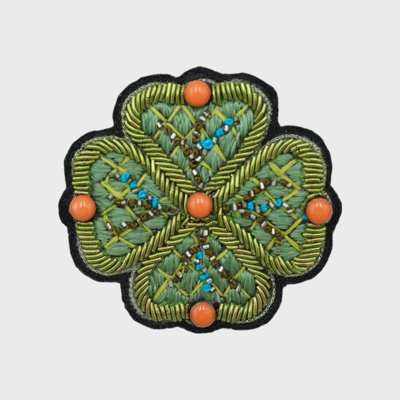 An embroidered brooch representing a green flower with blue and orange details.