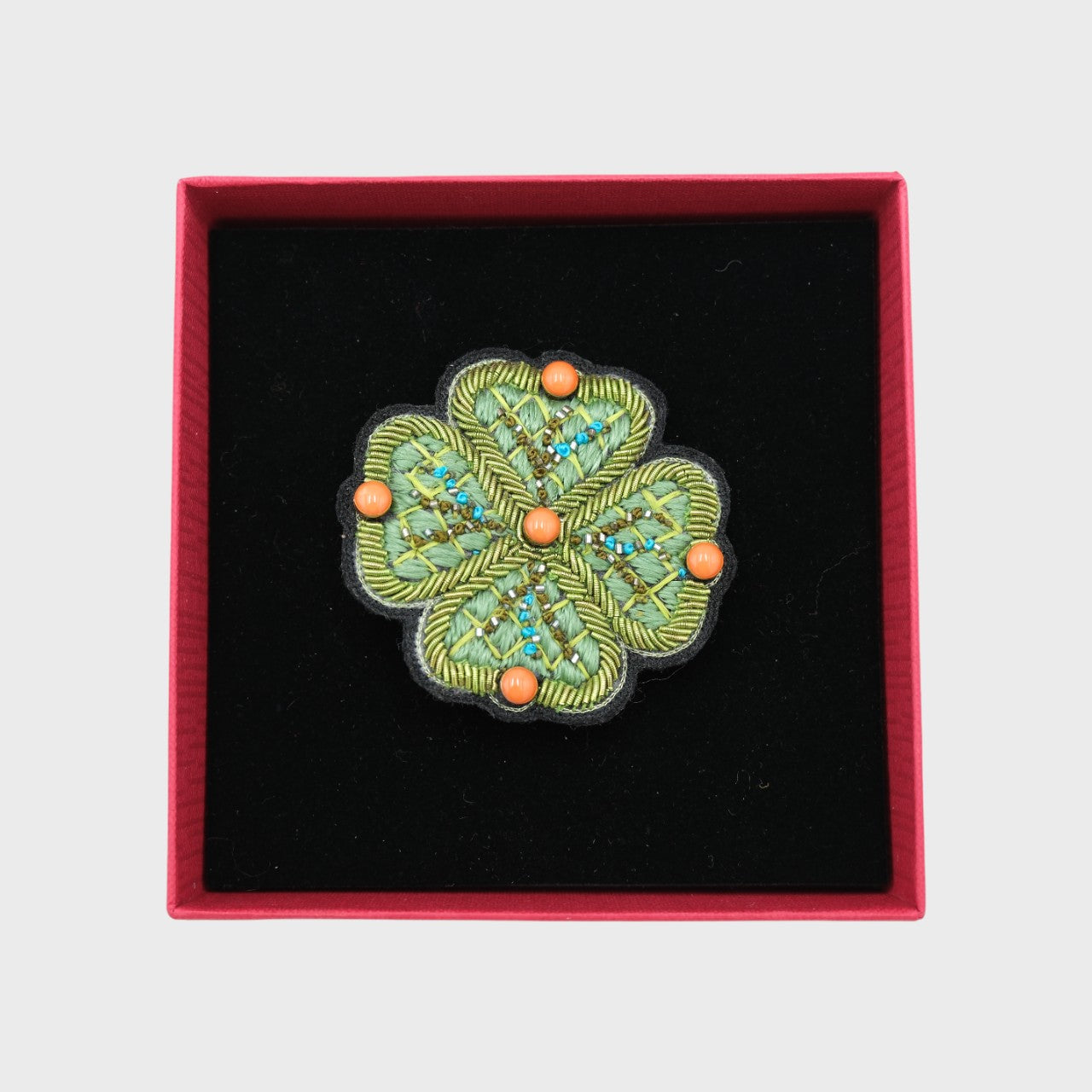 An embroidered brooch representing a green flower in a box.