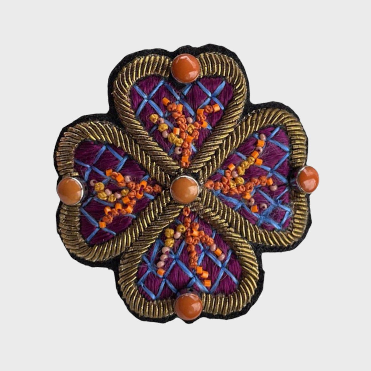 An embroidered brooch representing a purple flower, with orange and blue details.