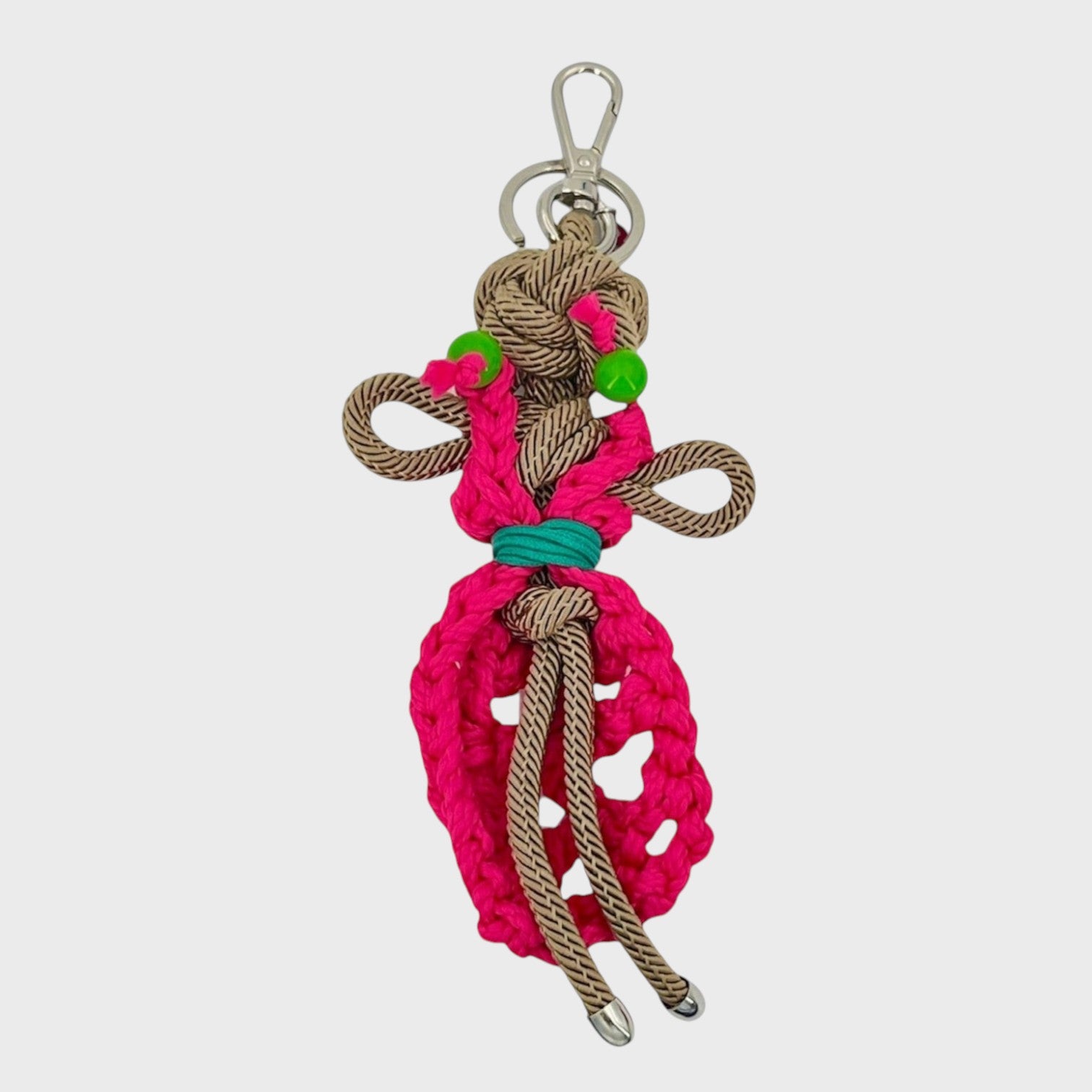 Handmade tan macramé bag charm featuring a female character, meant to represent a colourful dancer wearing a long pink dress and green earrings. She is attached to a silver clasp.