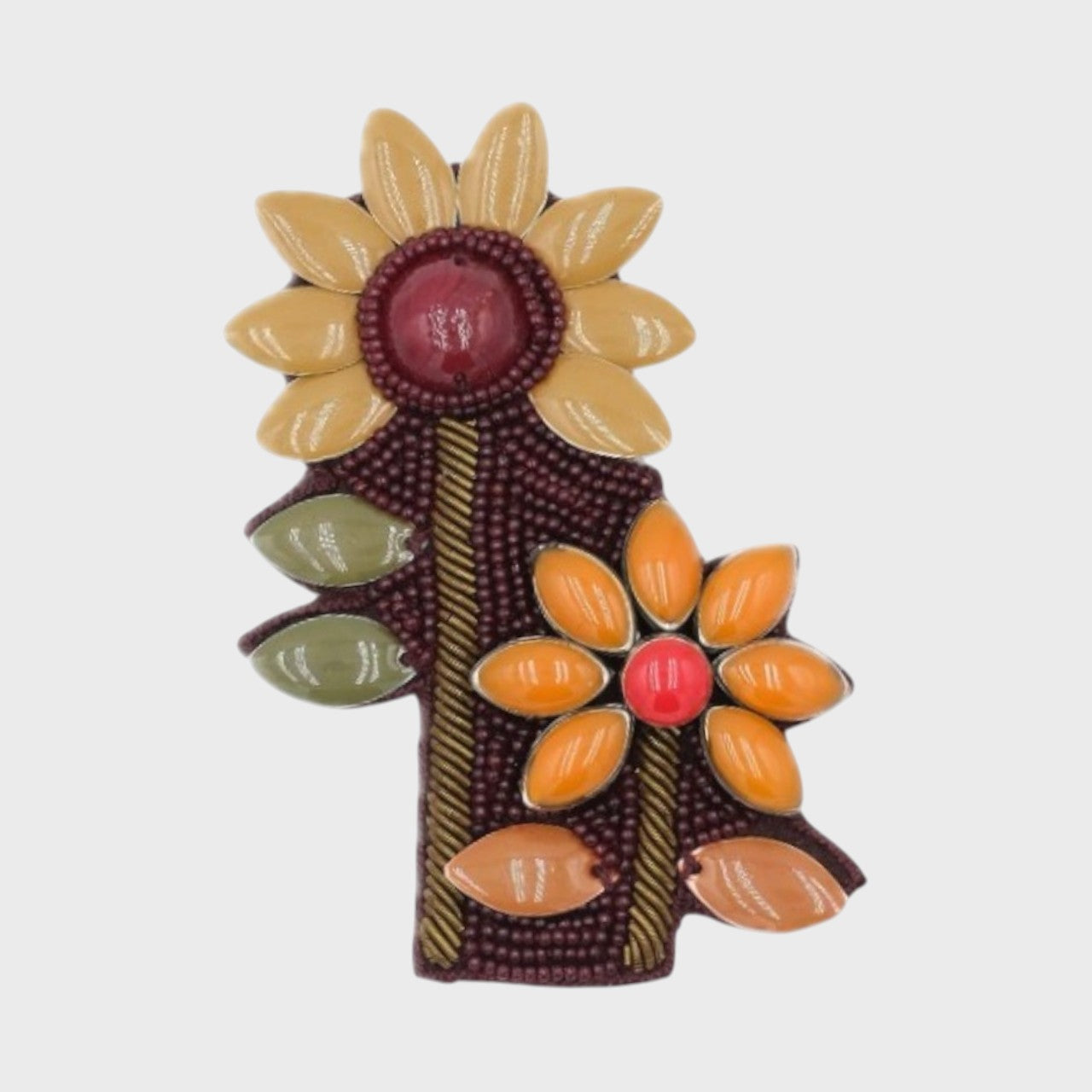 An embroidered brooch representing a manuka bouquet with red center and beige and yellow petals.