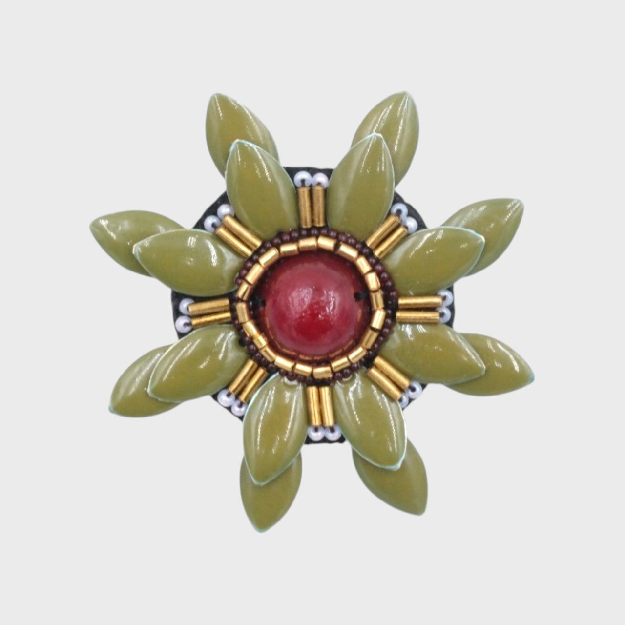 An embroidered brooch representing a manuka flower with green stone and red stone.