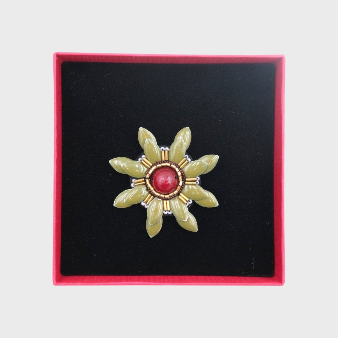 An embroidered brooch representing a green manuka flower in a box.