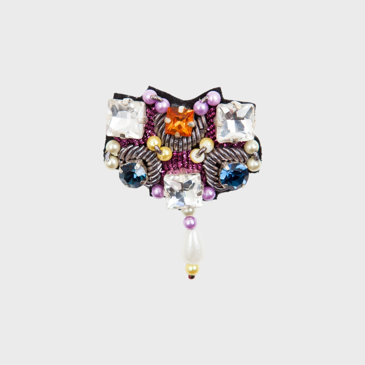 An embroidered brooch with white stones, pink, orange and blue details.