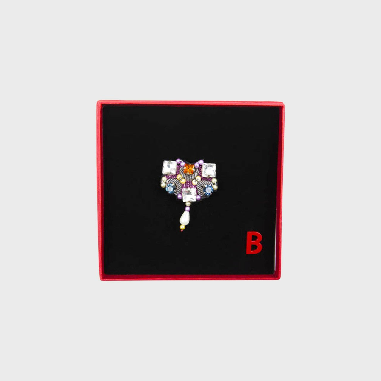 An embroidered brooch with white stones and pink details in a box.