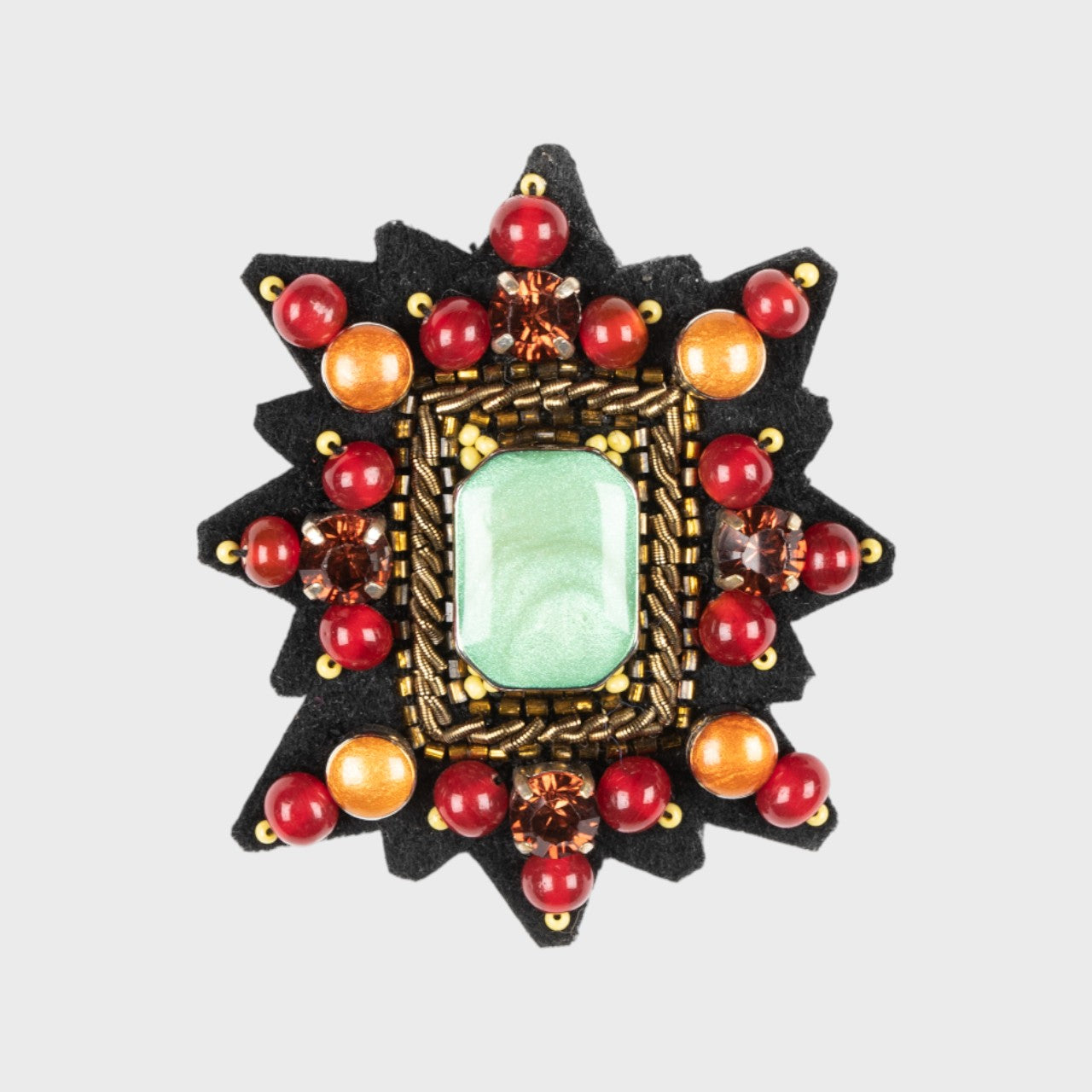 An Embroidered brooch representing a Mizar star with red and orange details and a green centered stone.