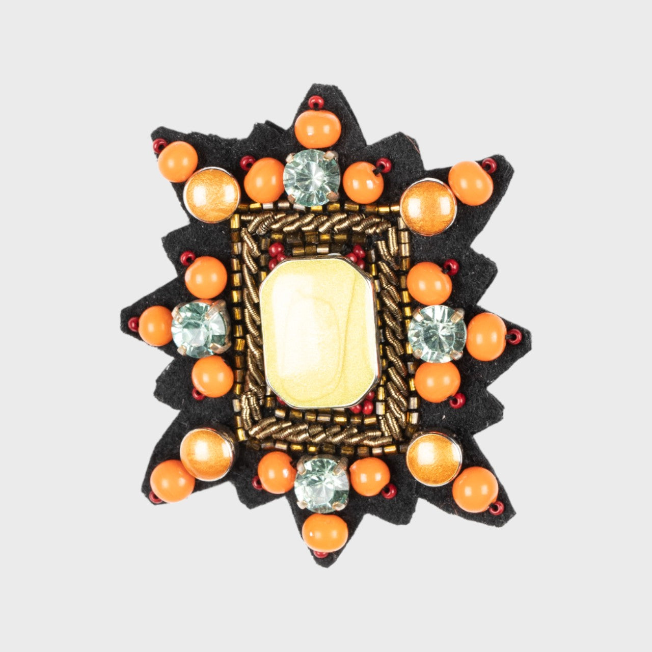 An embroidered brooch representing a Mizar strap with orange, yellow and white details.