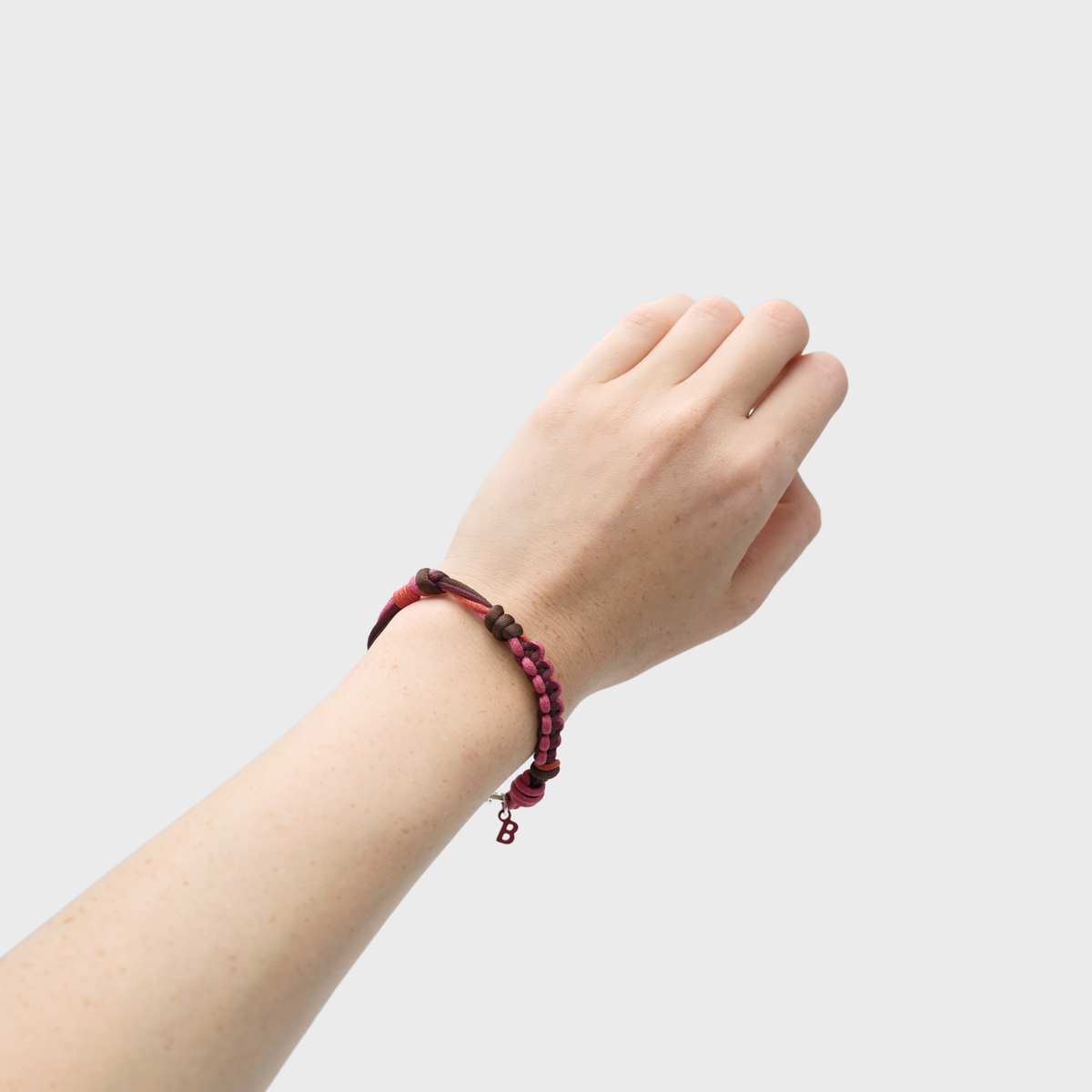 A close-up of a person's wrist wearing a dark red and brown beaded bracelet with a small hanging charm, set against a plain light gray background.