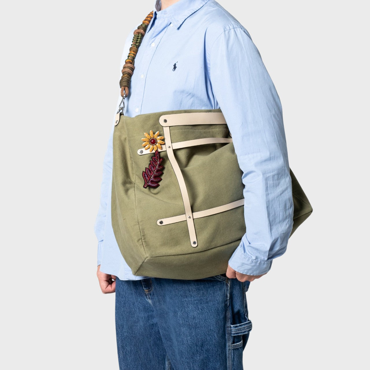 Multicolored braided macramé bag strap in dark green and brown, shown on a green cotton Candide Weekender bag held on a man's shoulders.