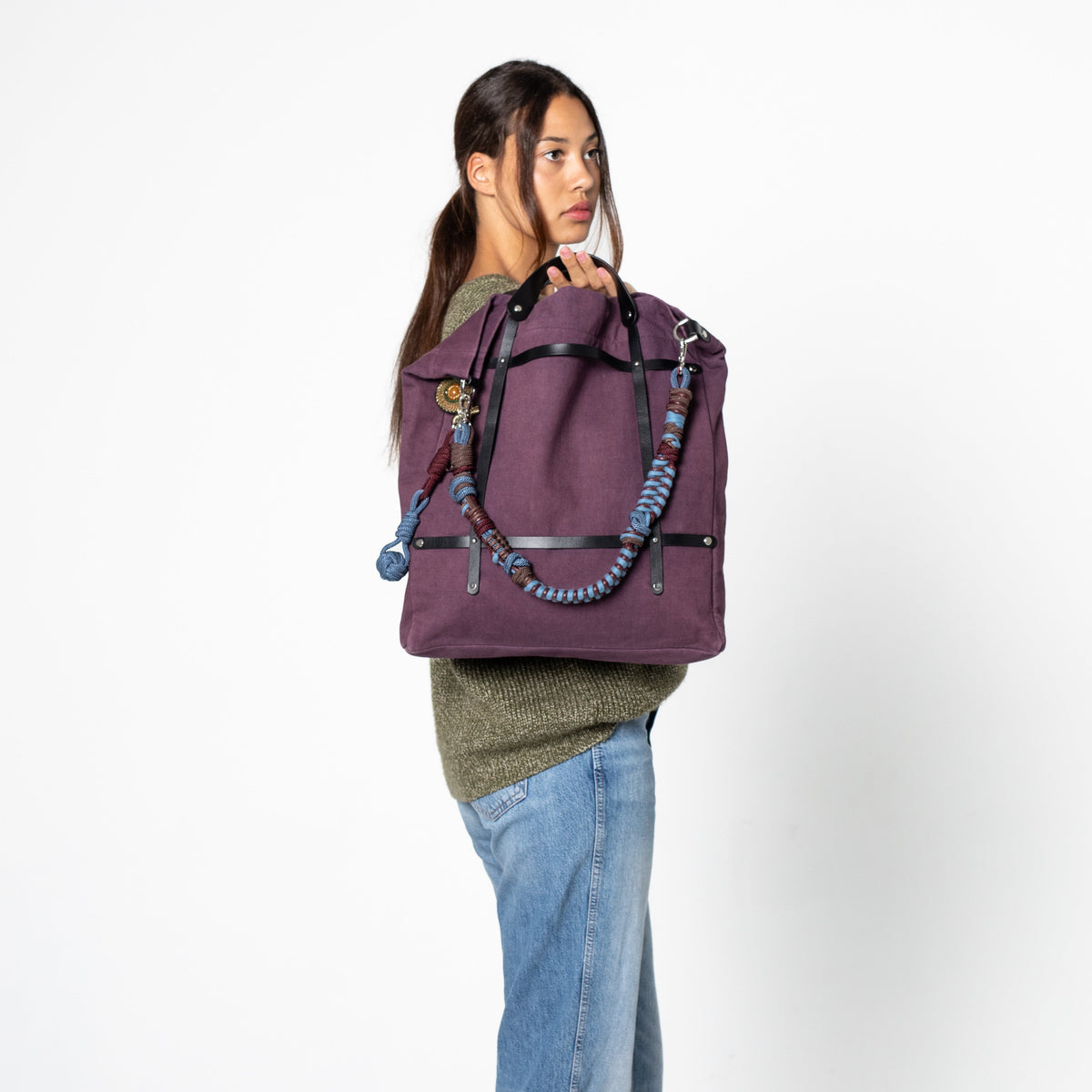 Person wearing a purple optimiste tote bag with a colourful macrame shoulder strap on a white background.
