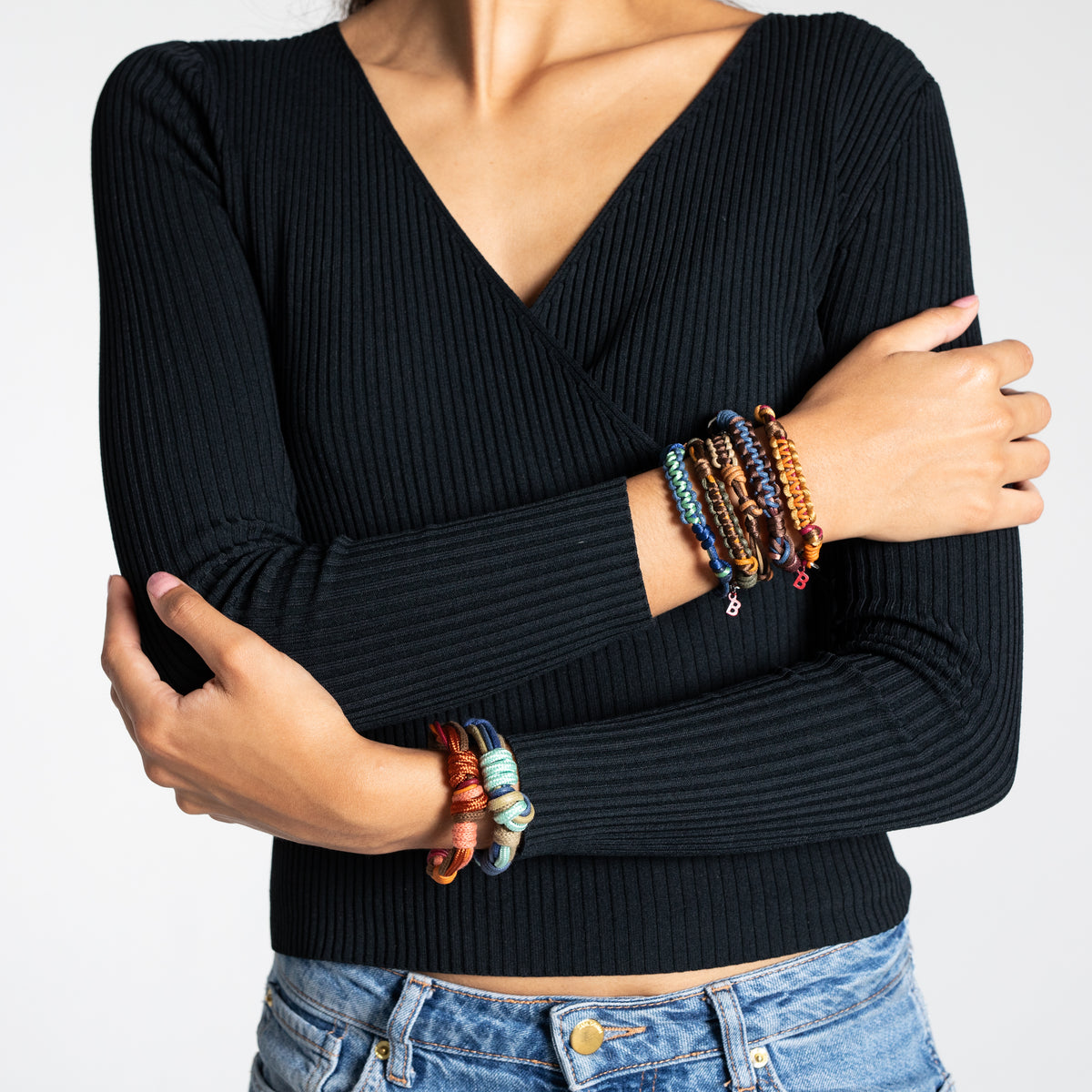 Person wearing a black ribbed sweater and colorful macramé woven bracelets on a plain background