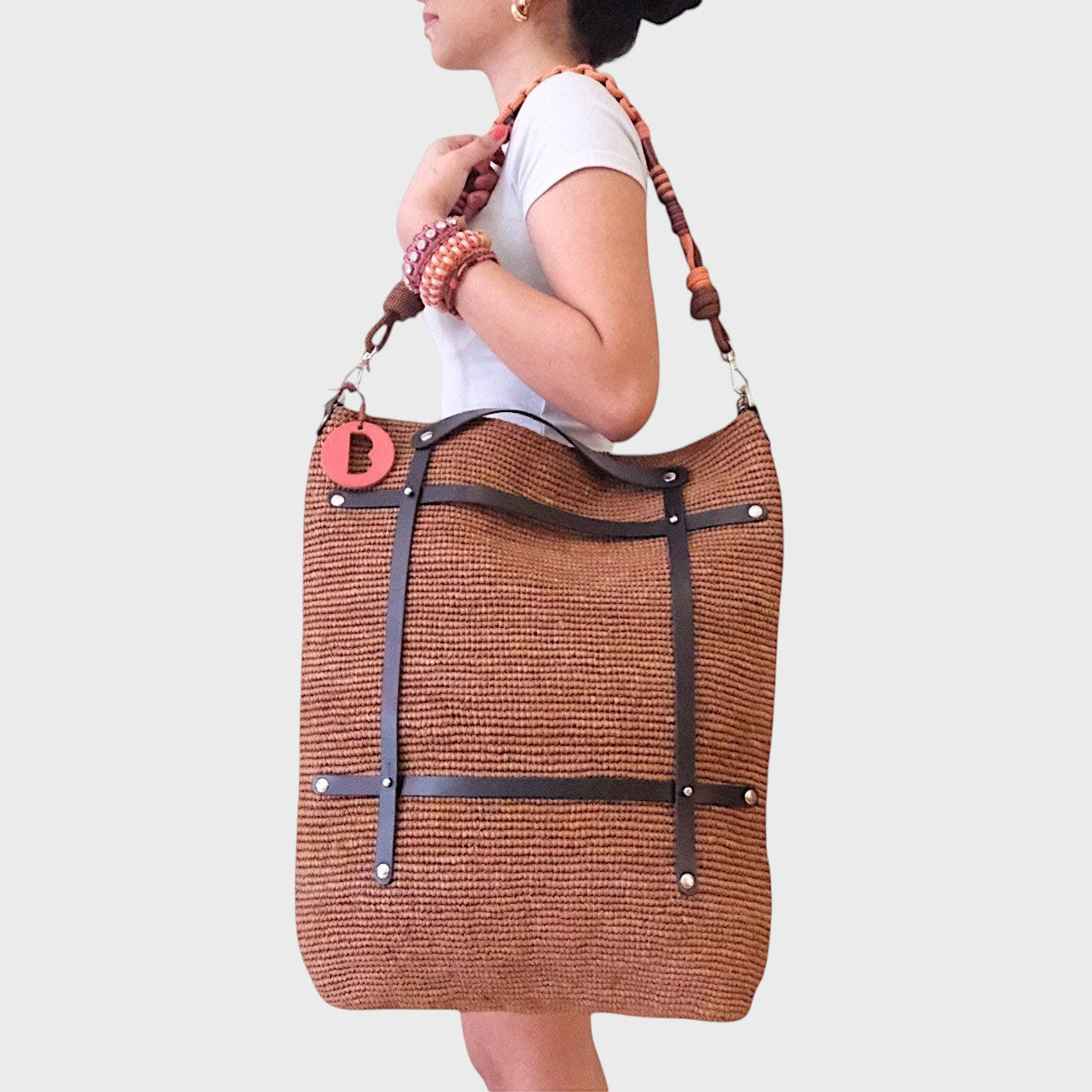 A model carrying on hr shoulder the brown raffia Optimiste tote bag with black leather