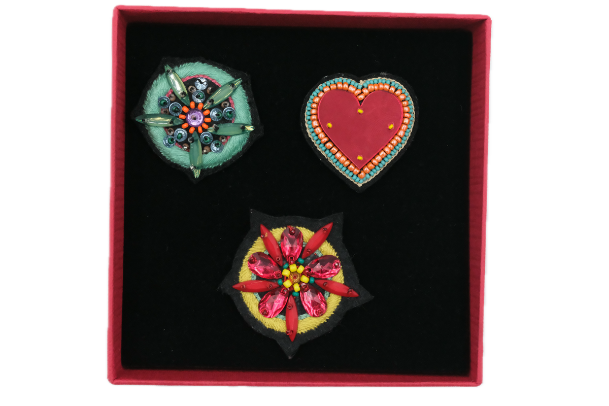 Three embroidered brooches, two flowers and one heart in a red box.
