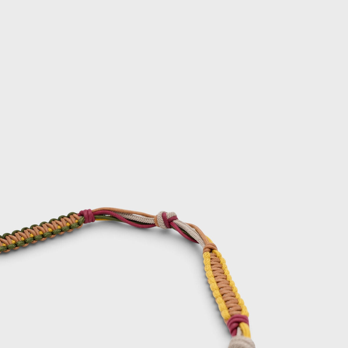 A detail of a macramé burgundy, yellow, brown and green bag strap.