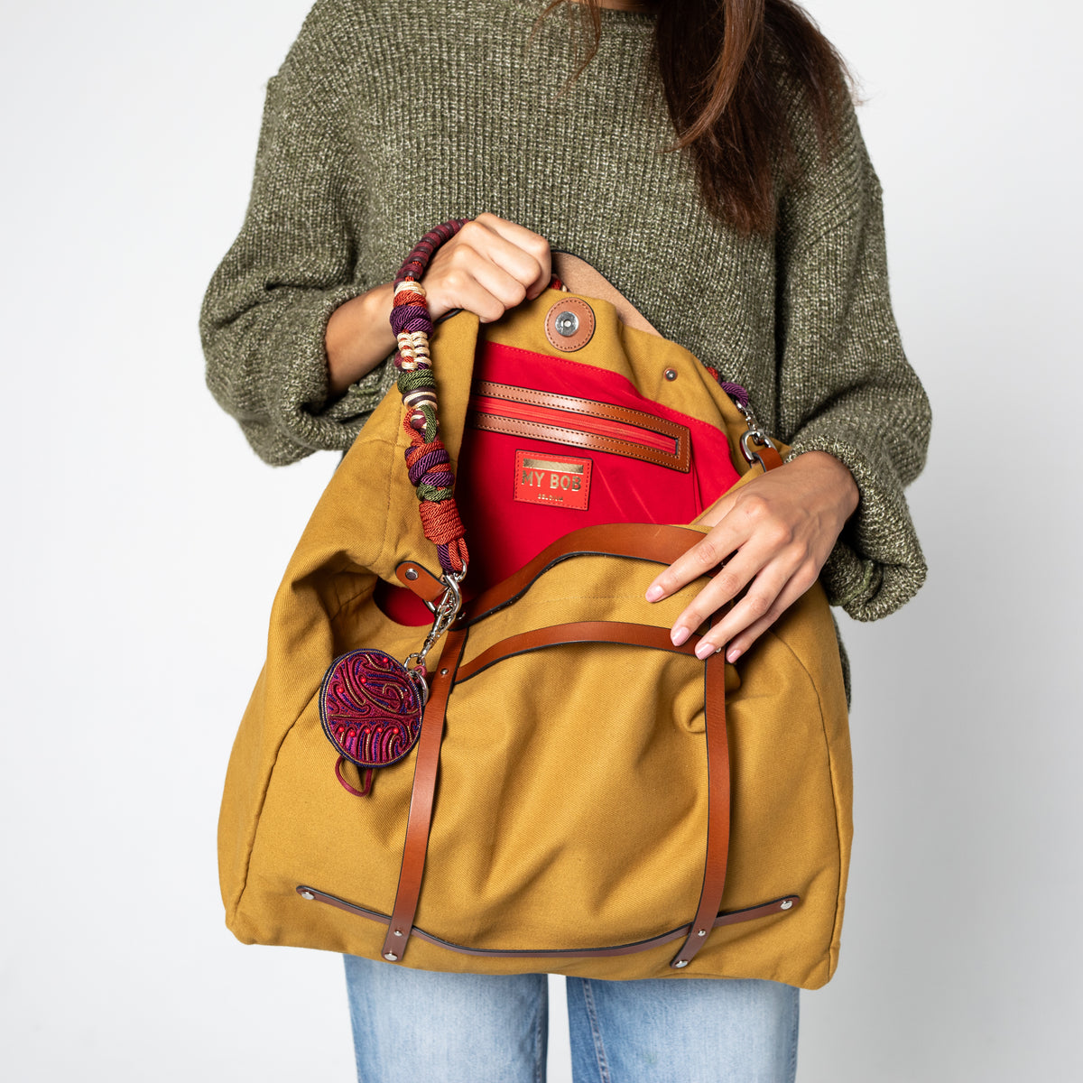 A person holding a mustard canva bag, showing the red inside of it.