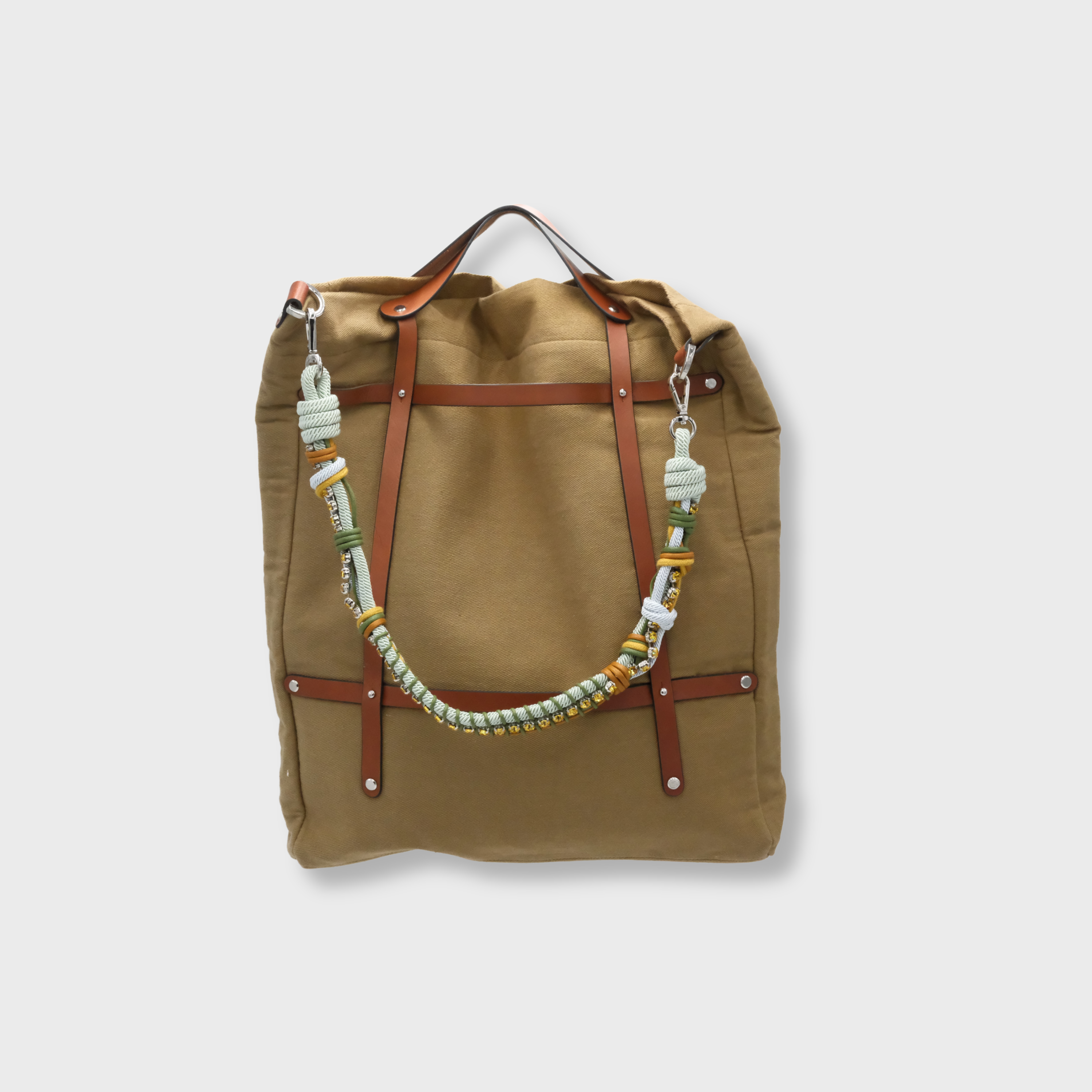A canvas tote bag in a Taupe color, featuring brown leather straps and a decorative beaded shoulder strap with green, white, and gold details.