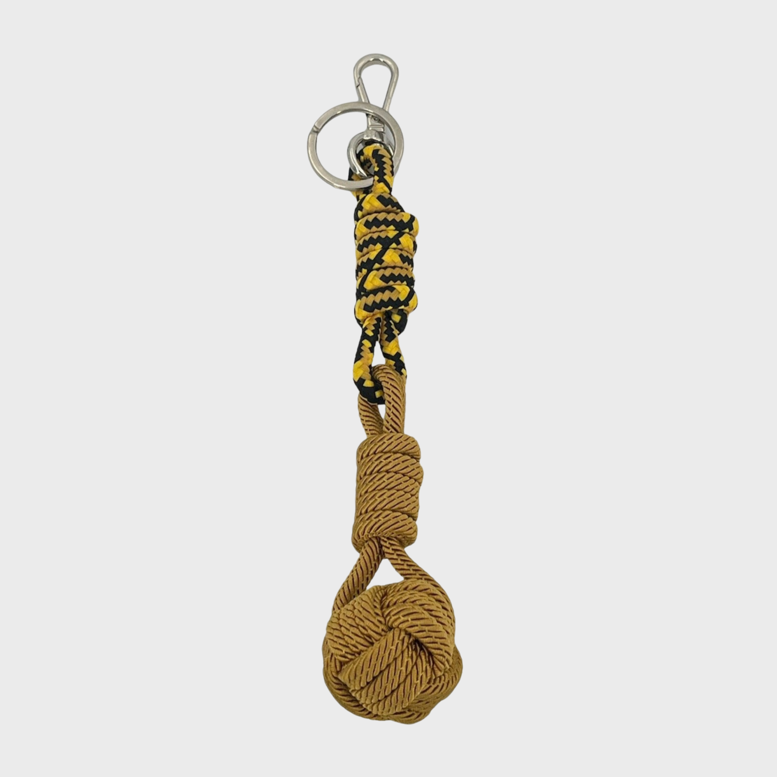 A macramé keychain representing a ball inspired by sailors knots. The straight upper part is black and mustard and the ball part is mustard yellow.