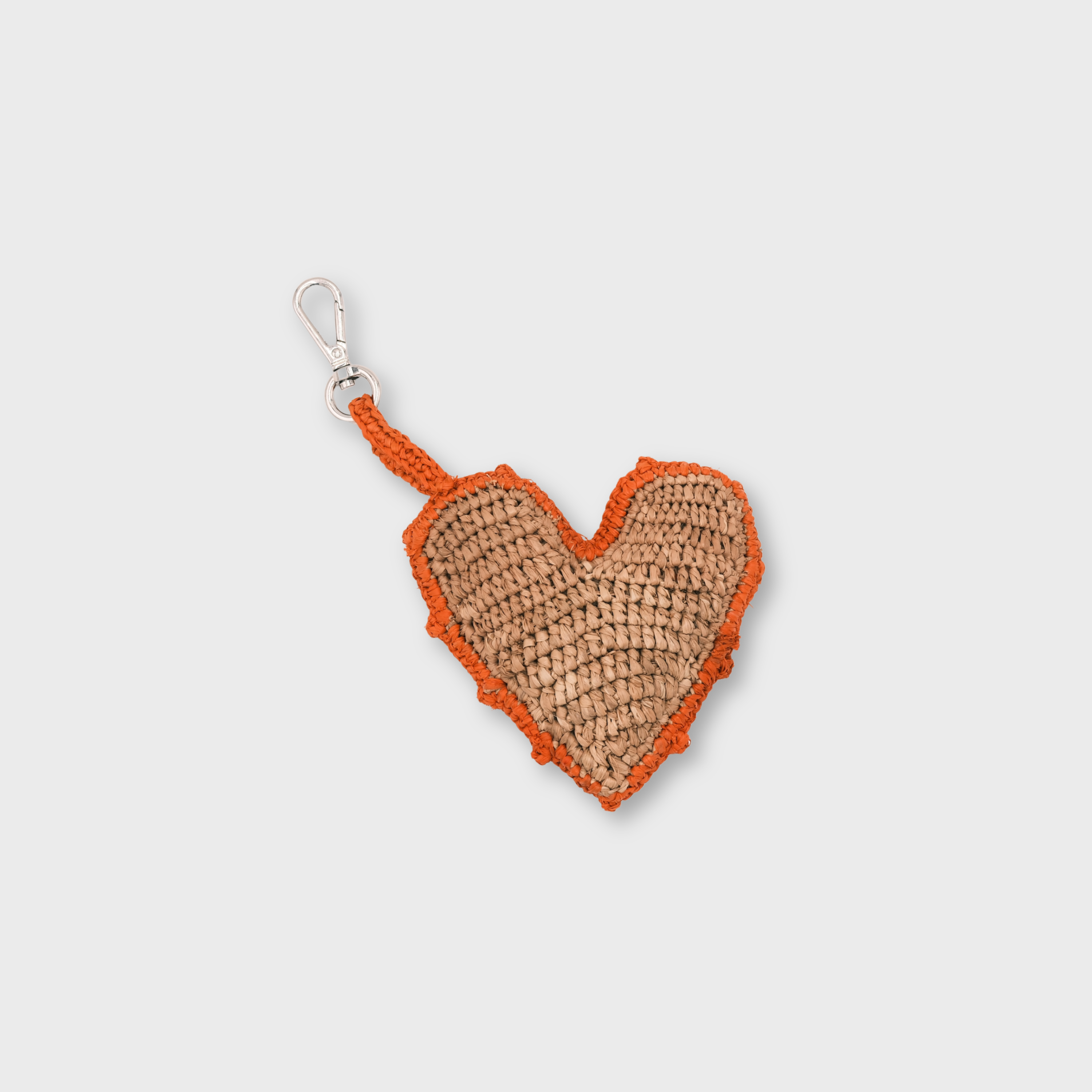 A heart-shaped raffia keychain in natural tan with an orange border and handle, attached to a silver metal clasp.