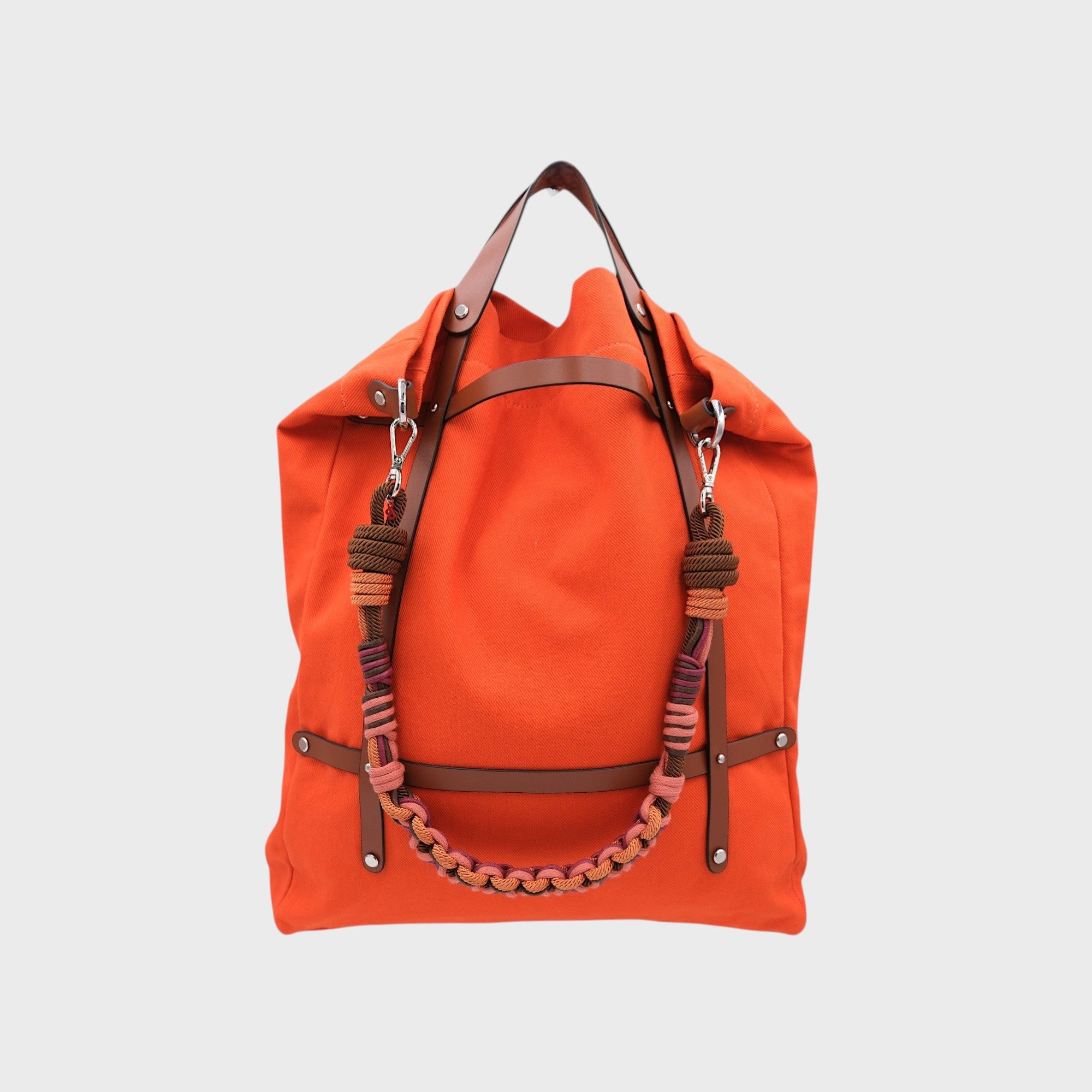 A canvas tote bag in an orange color, featuring brown leather straps and a decorative beaded shoulder strap with pink, orange and brown details.