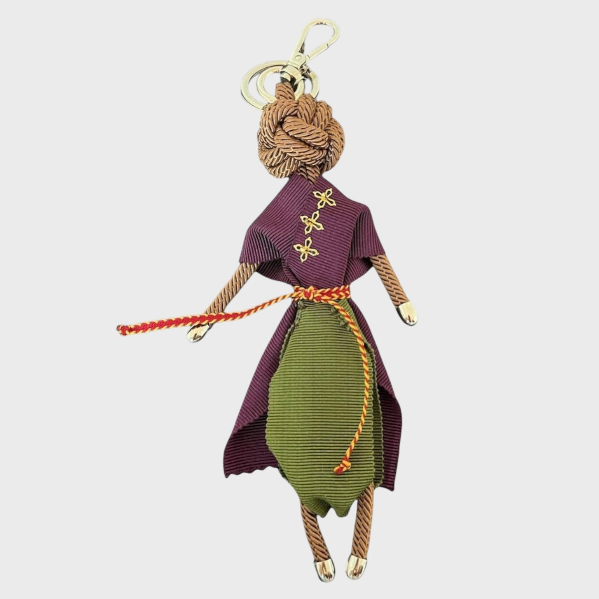 A macramé Keychain in the shape of a person wearing a purple outfit with green pants on a white background