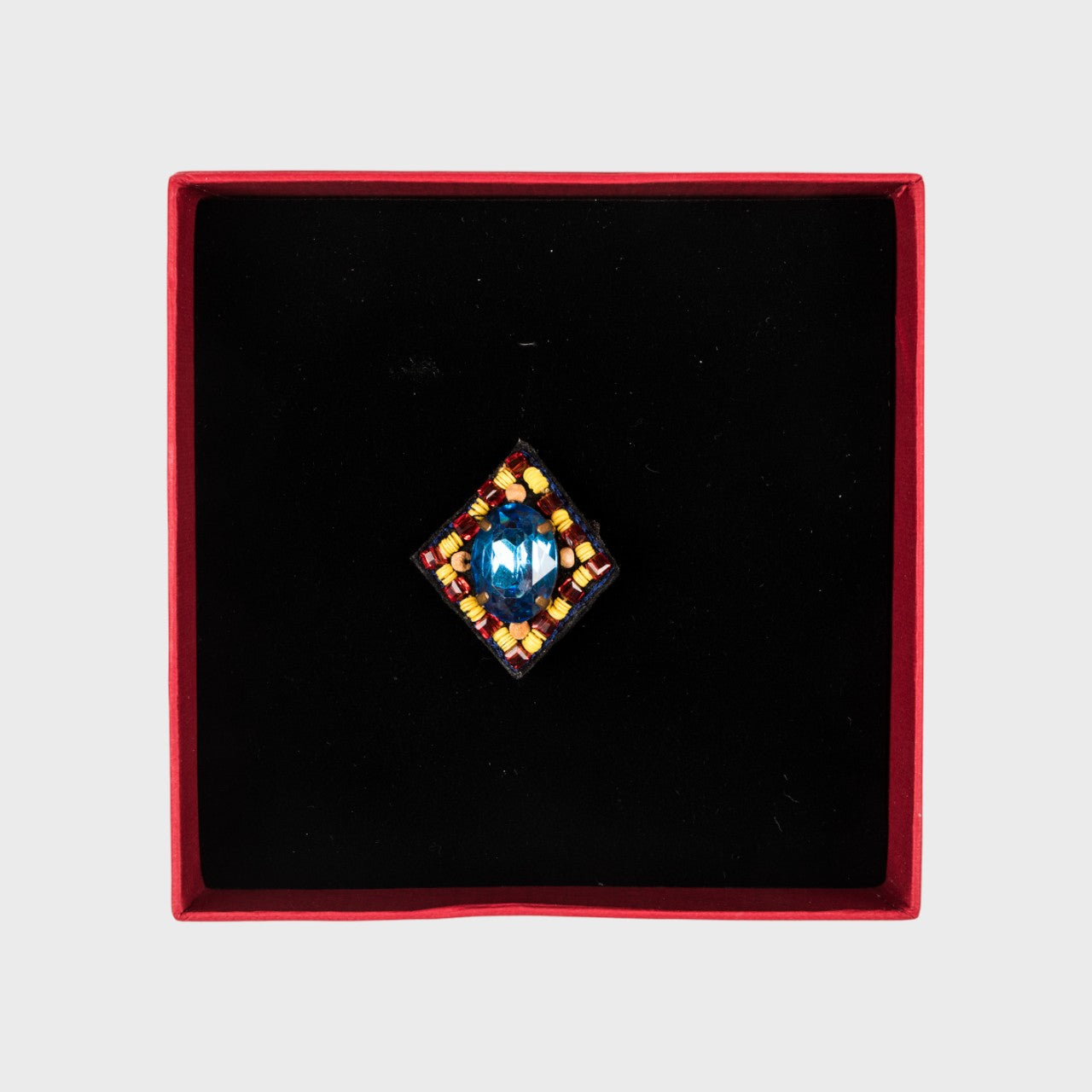 A blue oval embroidered brooch in a box.