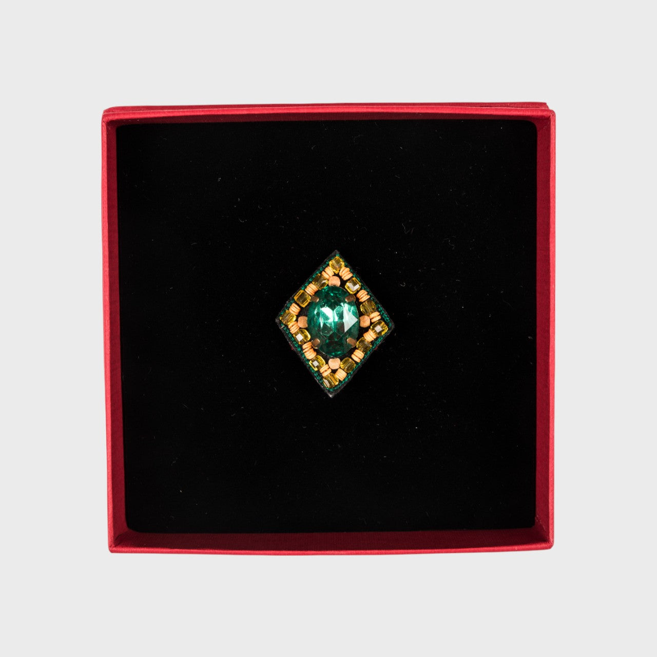 A green oval embroidered brooch in a box.