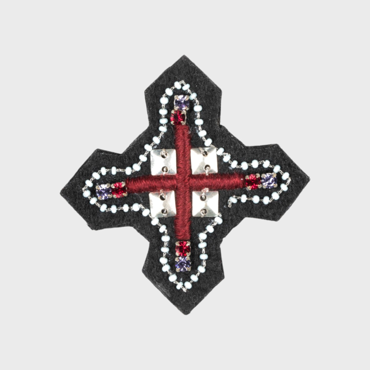 An embroidered brooch representing a red cross with white details around.