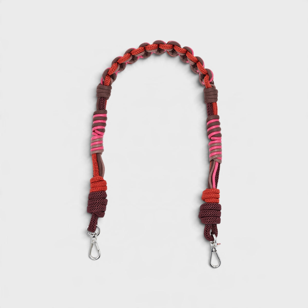 A macramé bag strap with red, pink and brown patterns.