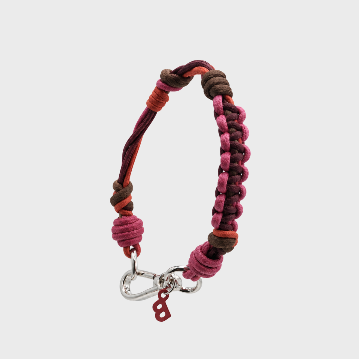 A handmade braided macrame bracelet with pink, brown, and orange cords, featuring a silver lobster clasp and a small red 'B' charm, shown on a light gray background.