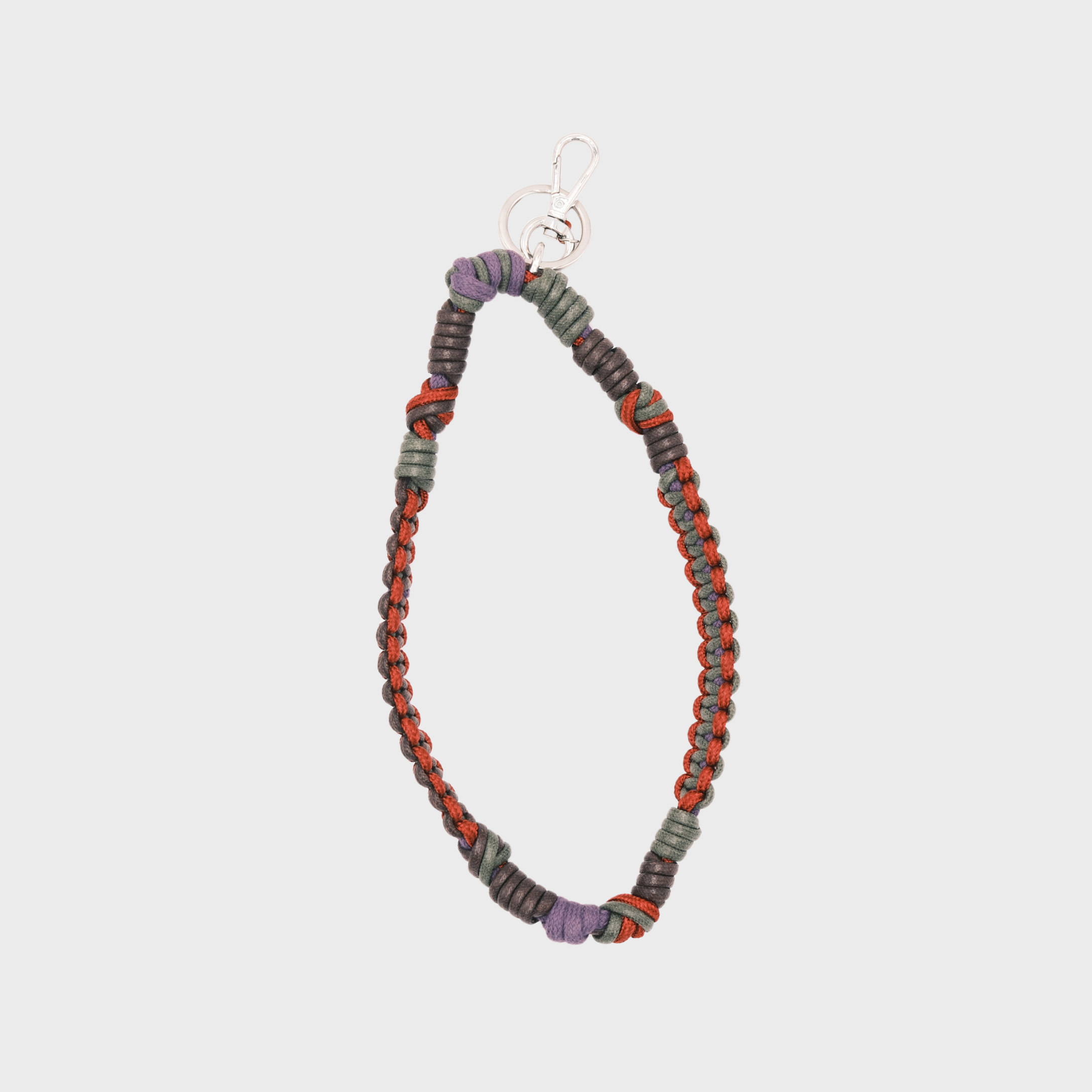 A bohemian-style woven macramé key chain with a silver-tone lobster clasp, featuring dark green, pink, purple and brown woven segments on a light gray background.