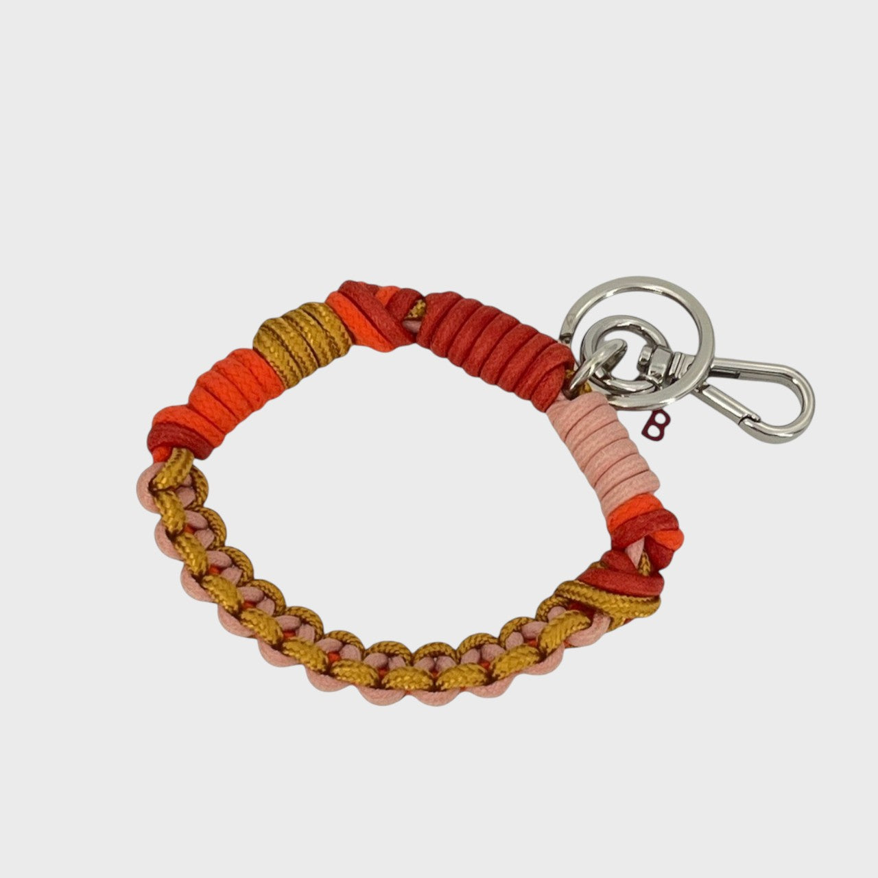 A woven macramé key chain with light pink, red, orange and yellow patterns, inspired by celtic knots, finished with silver-tone metal hardware.