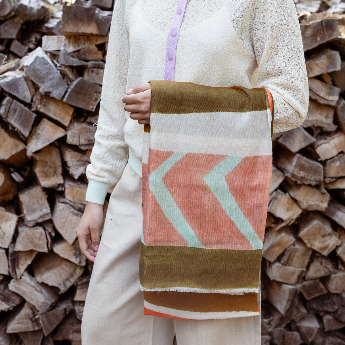Person holding a patterned cashmere shawl with stacked wood in the background
