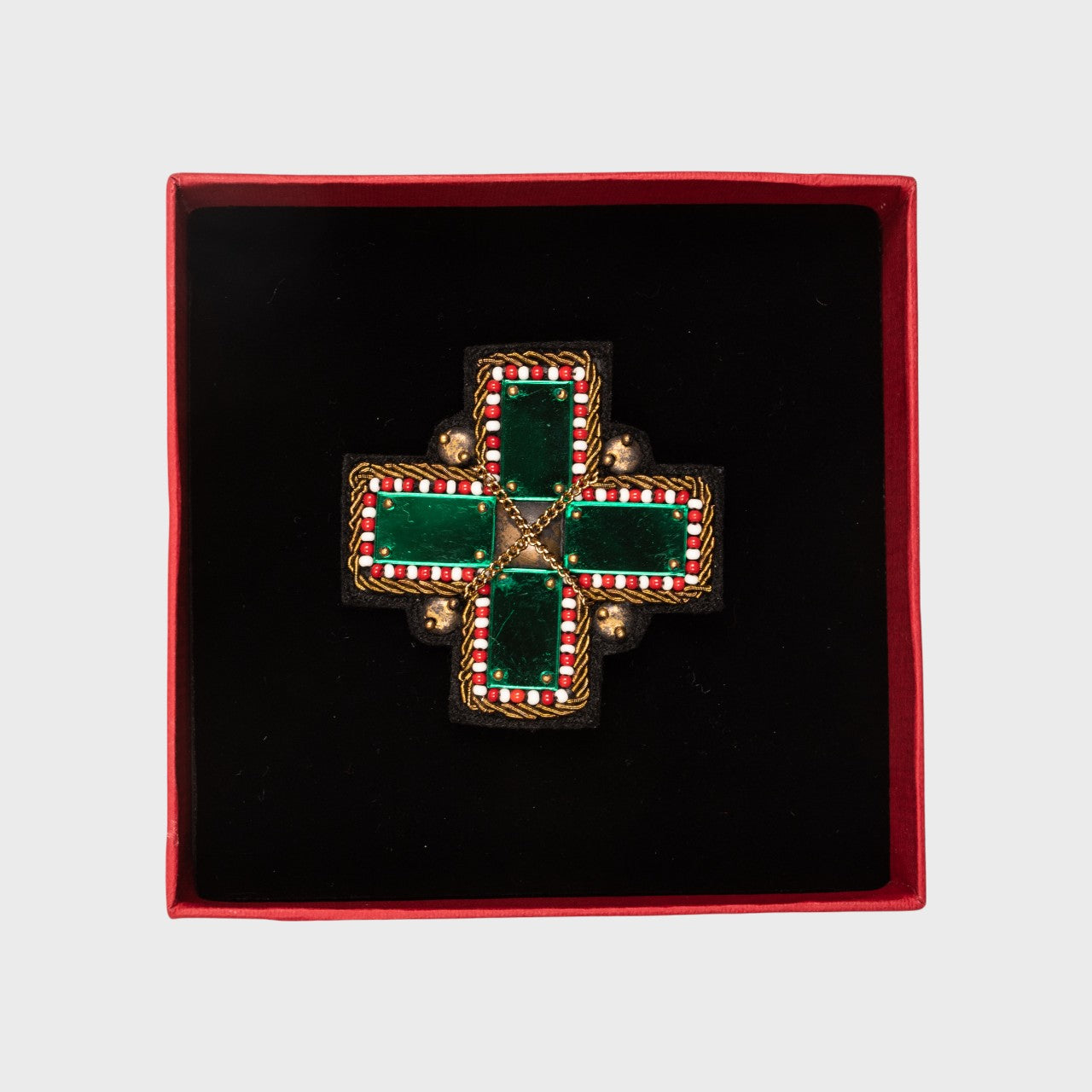 An embroidered brooch representing a green cross in a box.