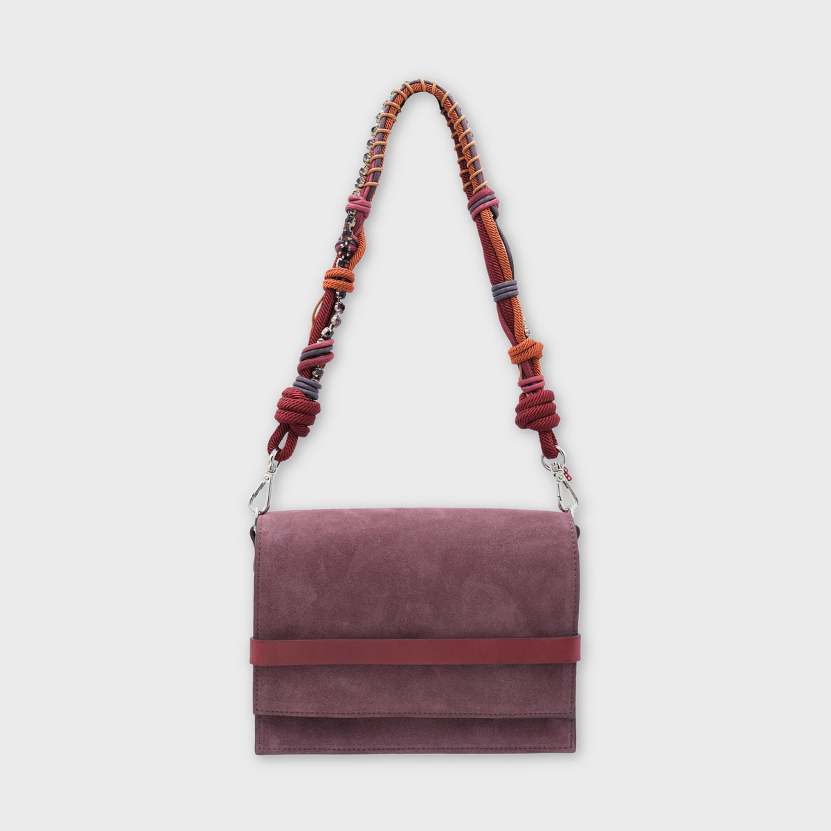 A rectangular suede shoulder flap bag in dusty mauve with a horizontal reddish-brown band across the front and a braided multicolor shoulder strap, shown against a light gray background.