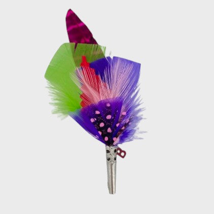Purple, green and pink feathered brooch on a light gray background