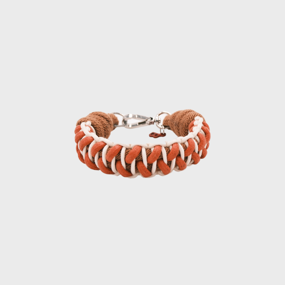 A braided macramé bracelet with shades of red, white and brown. It ends and a silver clasp, shown on a light gray background.