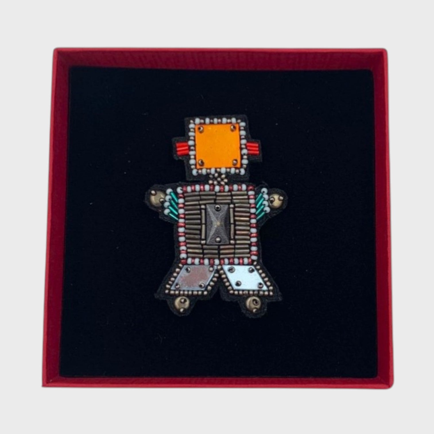 An embroidered robot brooch on a red box.