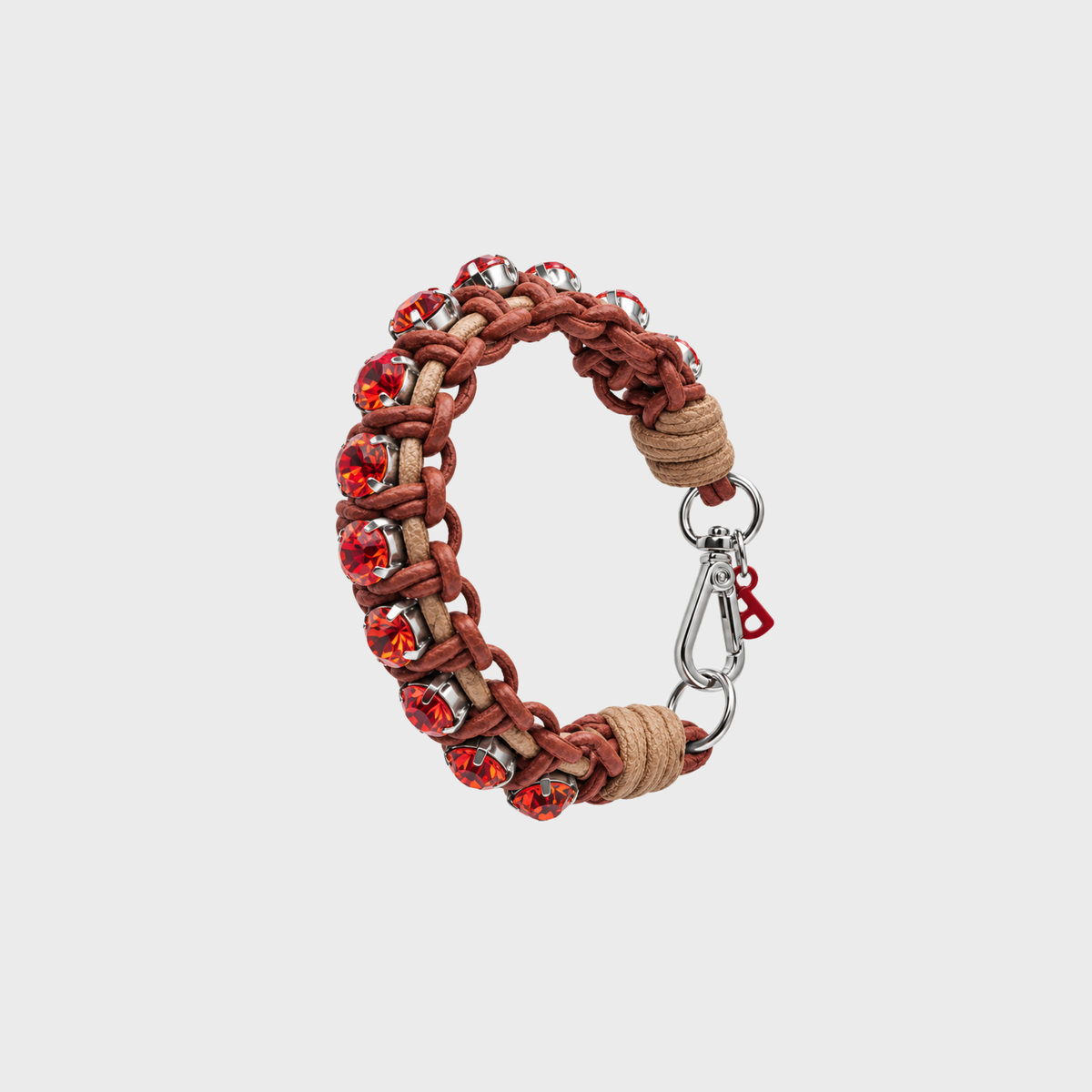 A braided macrame bracelet with alternating brown and tan woven sections, accented by faceted red crystal beads and a silver lobster clasp with a small red B tag, shown on a light gray background.