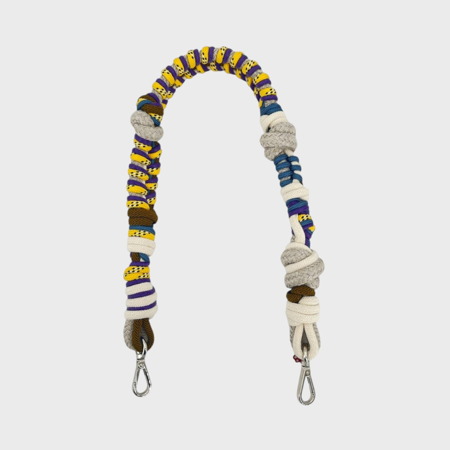Multicolored braided macramé bag strap in bright yellow, dark green and purple, with white, shown on a light gray background.