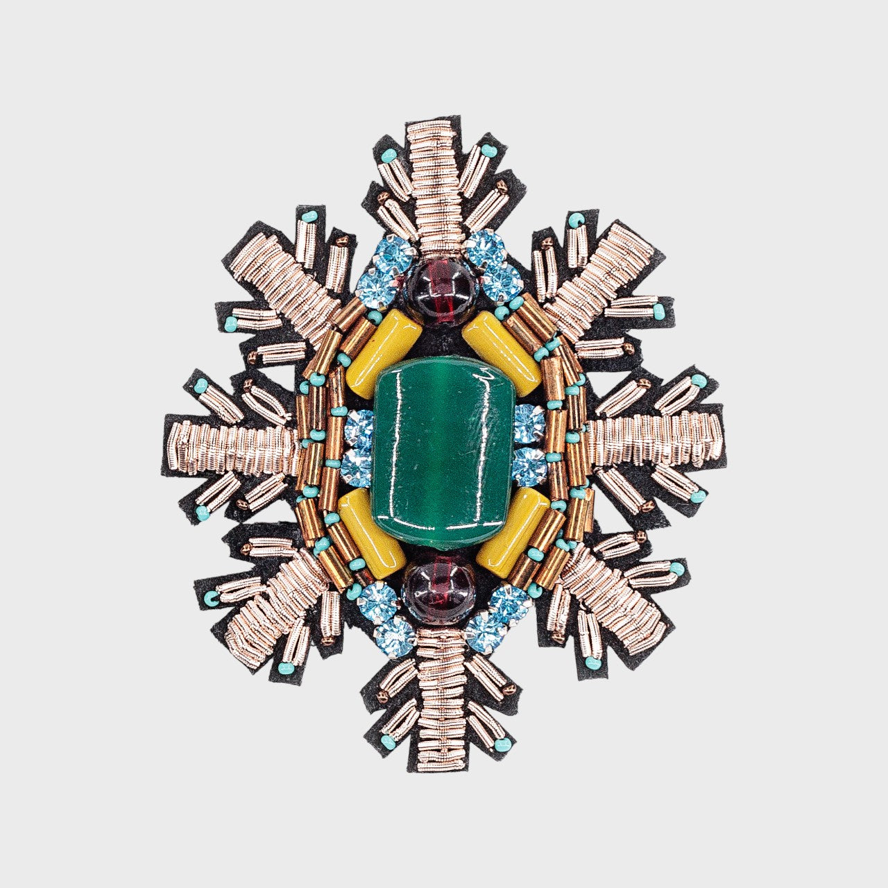 An embroidered brooch representing a snowflake with a green stoned center and blue, silver and green details.