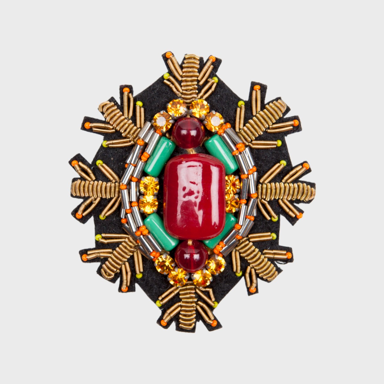 An embroidered brooch representing a snowflake with a red stoned center and golden details.