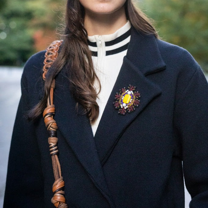 A model wearing a snowflake brooch with a yellow stoned middle and pink and purple details.